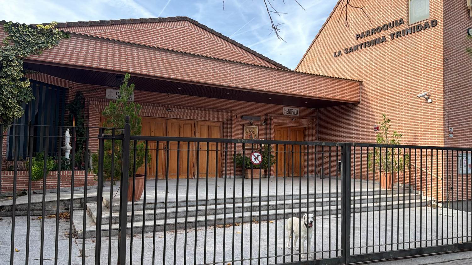 Fachada de la parroquia Santísima Trinidad, con la entrada y la imagen de la Virgen; un perro blanco espera ante la verja