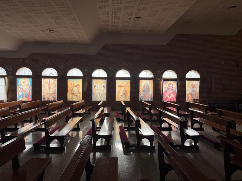 Vidrieras de la parroquia con imágenes de Cristo y de los ángeles, entre los bancos